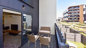 A balcony with wicker furniture, a TV, and a view of a modern building complex. - Stylish 2BR Retreat by Te Kaha Stadium (Christchurch)