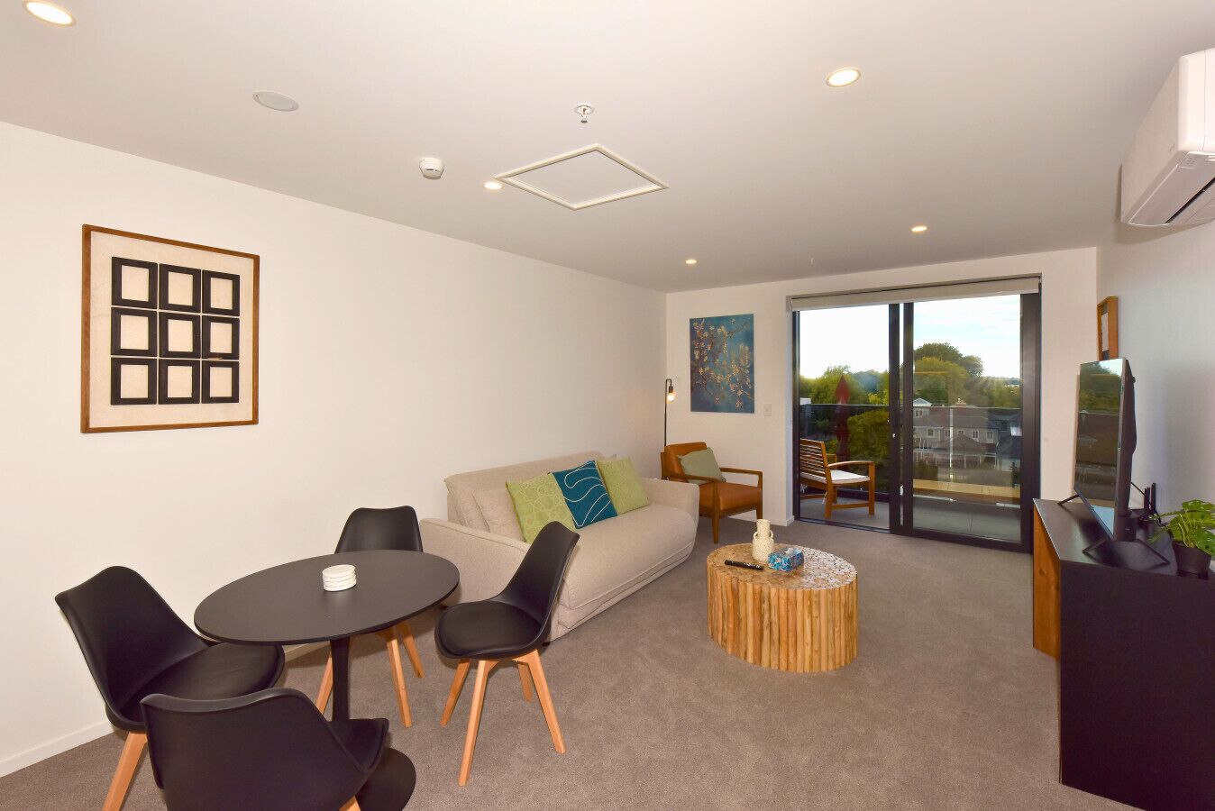 A modern living room with a sofa, chairs, a round coffee table, and a balcony with a view.