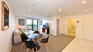 A modern living room with a sofa, chairs, a table, and a TV. - Fresh 1 Bedroom Apartment Close to Te Kaha Stadium (Christchurch)