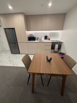 Eine moderne Küche mit eingebauter Mikrowelle, Herd und Backofen. Ein Esstisch mit zwei Stühlen und einer schwarzen Vase steht daneben.