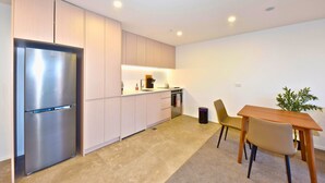 Eine moderne Küche mit einem Edelstahl-Kühlschrank, hellem Küchenschrank und einem kleinen Essbereich mit Holztisch und Stühlen. Eine Topfpflanze steht ebenfalls da.