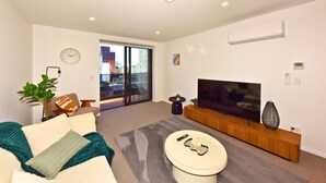 Ein modernes Wohnzimmer mit Flachbildfernseher, einer Couch, einem Couchtisch und Blick durch eine Glastür nach draußen.