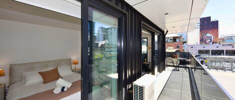 A modern hotel room with a large bed, a glass wall, and a view of the city.