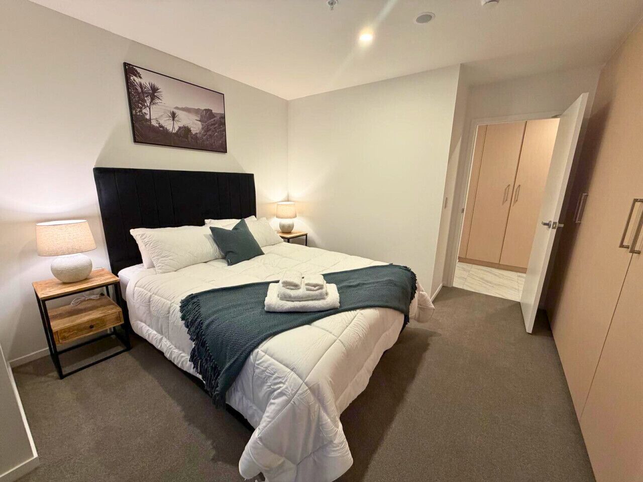 A bedroom with a bed, bedside tables, a nightstand, a door, and a wall-mounted picture.