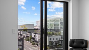 Een moderne kamer met een groot raam, een zwarte lederen fauteuil en uitzicht op een stadsgezicht met gebouwen en een heldere lucht.
