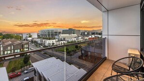 Een balkon met uitzicht op een stadsgezicht tijdens zonsondergang, met moderne gebouwen en een stadion.