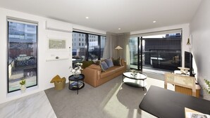 A modern living room with a sofa, coffee table, and a dining area. - Free Carpark & Stylish City Apartment Near Te Kaha (Christchurch)