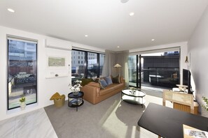 A modern living room with a sofa, coffee table, and a dining area. - Stylish City Apartment Near Te Kaha (Christchurch)