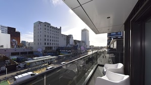A modern building with a glass balcony overlooking a busy street with a tram and buses. - Free Carpark & Stylish City Apartment Near Te Kaha (Christchurch)