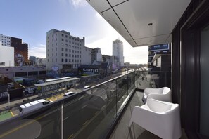 A modern building with a glass balcony overlooking a busy street with a tram and buses. - Stylish City Apartment Near Te Kaha (Christchurch)