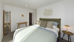 A bedroom with a bed, bedside table, lamp, and a mirror. - Free Carpark & Stylish City Apartment Near Te Kaha (Christchurch)