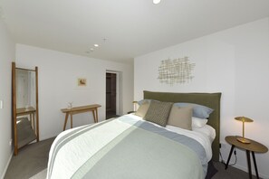 A bedroom with a bed, bedside table, lamp, and a mirror. - Free Carpark & Stylish City Apartment Near Te Kaha (Christchurch)