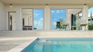 A modern outdoor pool area with a clear view of the sky, a seating area with chairs, and a pathway leading to a door.