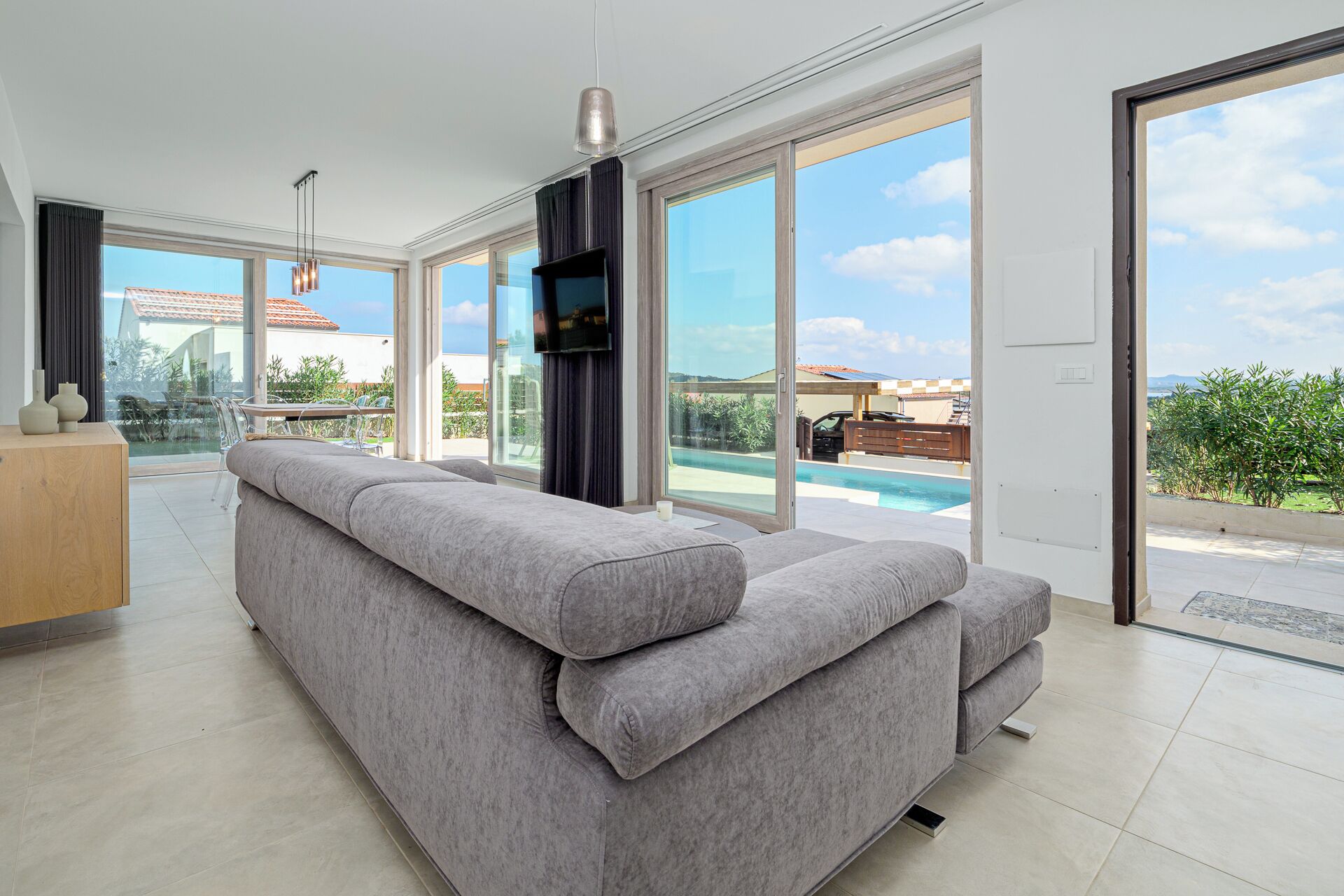 A modern living room with a grey sectional sofa, large windows, and a view of a swimming pool.