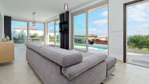 A modern living room with a grey sectional sofa, large windows, and a view of a swimming pool.