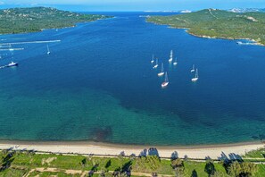 An aerial view of a coastal area with clear blue waters, several sailboats, and a sandy beach. - Villa Luce – new and modern villa with pool in sunny Sardinia (Porto Pozzo)