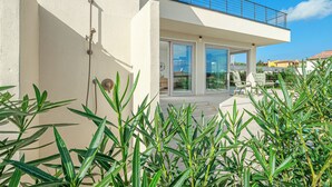A modern house with a balcony, large windows, and a patio area with outdoor furniture.