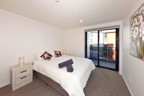 A bedroom with a bed, nightstands, a lamp, a painting, and a sliding glass door to the outside.