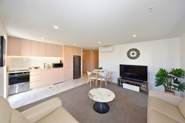A modern apartment with a kitchen, dining area, living room, and a TV.