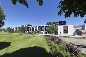 A modern building with multiple floors, a flat roof, and a well-maintained lawn with various plants.