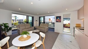 Una sala moderna con un conjunto de sofá, una mesa de comedor y sillas, una mesita redonda con una planta y una zona de cocina con ventana.