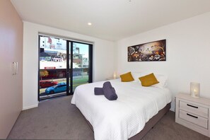 A bedroom with a large bed, a painting, a nightstand, and a view through a glass door. - 2 Bedroom Delight near Te Kaha Stadium (Christchurch)