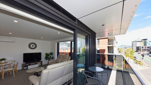 Una sala de estar moderna con sofá, televisor y comedor, un balcón con vistas a la ciudad.