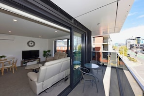 A modern living room with a sofa, TV, and dining area, a balcony with a view of the city.