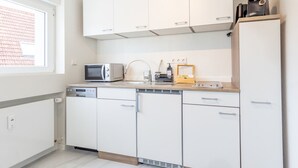 Una cocina moderna con armarios blancos, microondas, cafetera y lavavajillas.