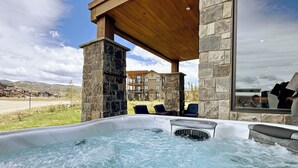 A hot tub with a stone structure, wooden roof, and a view of a multi-story building in the background. - Springview Meadows: Lux Condo with Private Hot Tub, Near Trails & Winter Park (Fraser)