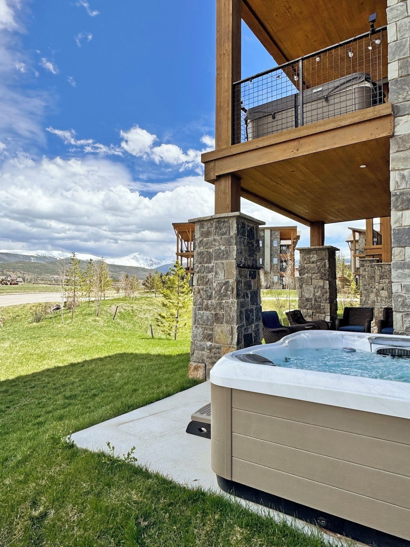 A hot tub in a backyard with a stone and wood structure, a clear sky, and a distant mountain range.