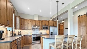 A modern kitchen with wooden cabinets, stainless steel appliances, and a central island with bar stools. - Springview Meadows: Lux Condo with Private Hot Tub, Near Trails & Winter Park (Fraser)