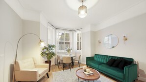 Un salon moderne avec un canapé vert, un fauteuil beige, une table basse ronde et un coin repas comprenant une table et des chaises.