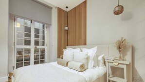 Une chambre avec un grand lit, un mur recouvert de lambris en bois, une petite table de chevet blanche et un luminaire suspendu.