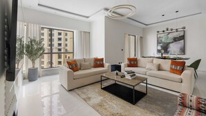 A modern living room with two sofas, a coffee table, and a large window offering a city view. - 2BR Marina View Steps from the Beach (Dubai)
