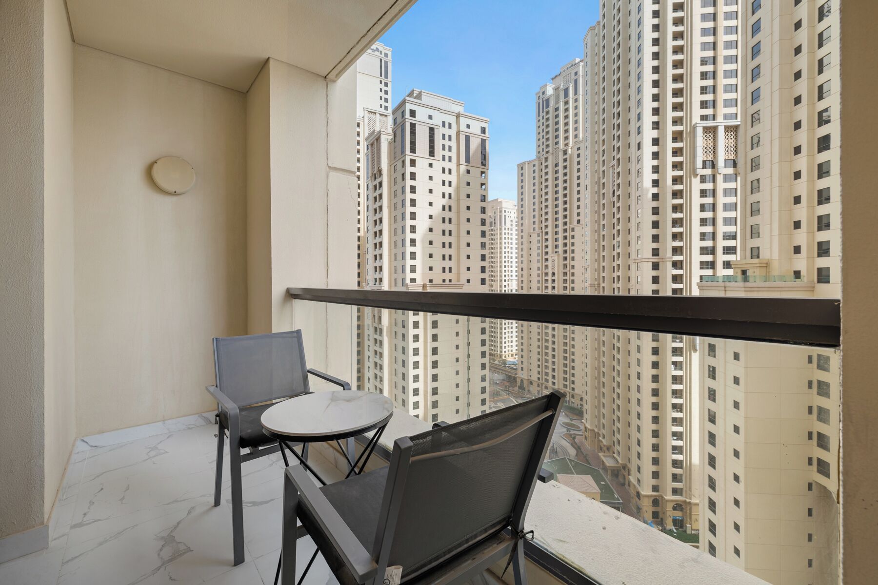 Un balcon avec deux chaises et une petite table, donnant sur de grands immeubles d’habitation.