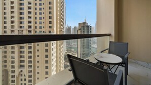 A balcony with a table and chairs, overlooking a cityscape with tall buildings. - 2BR Marina View Steps from the Beach (Dubai)