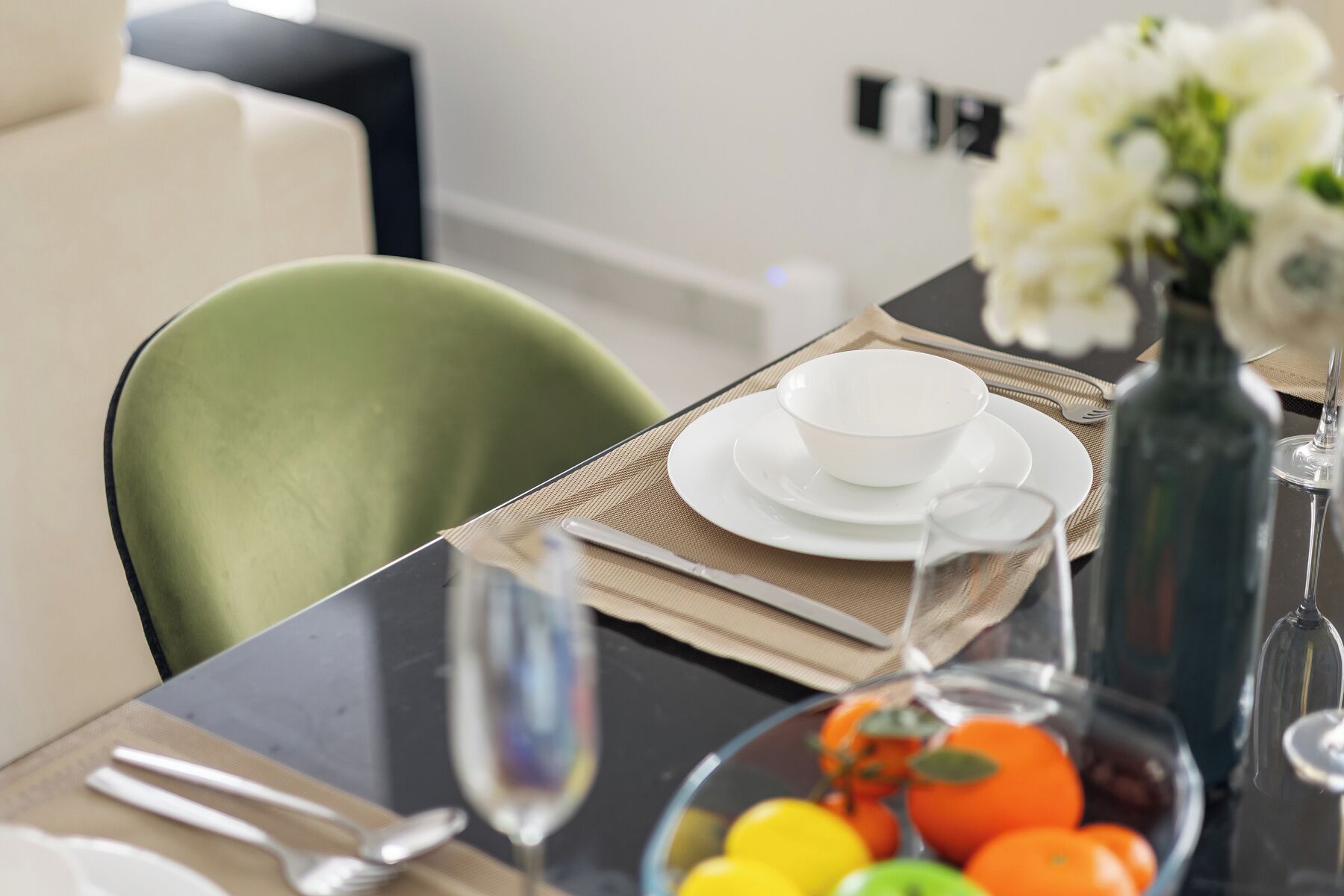 A dining table with a white bowl, a glass of water, and a bowl of fruit.