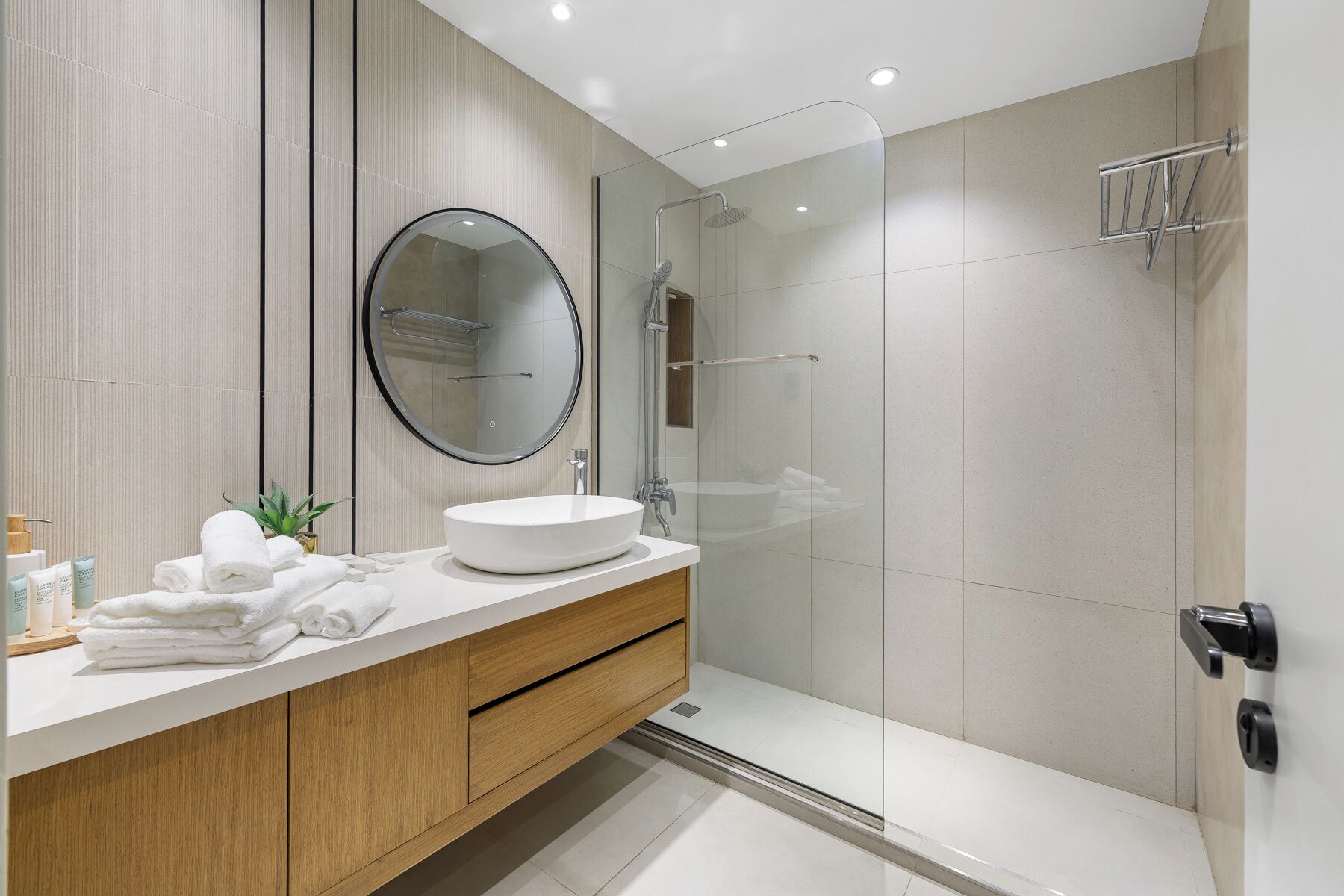 A modern bathroom with a round mirror, a white sink, and a glass shower enclosure.