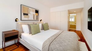 A bedroom with a bed, bedside tables, a framed abstract artwork, a wardrobe, and a shower area. - Modern Flat in Central Lisbon (Lisbon)
