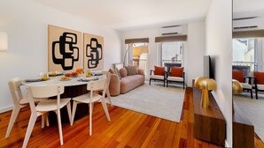 A modern living room with a dining area, featuring a wooden floor, a sofa, a TV, and abstract wall art. - Modern Flat in Central Lisbon (Lisbon)