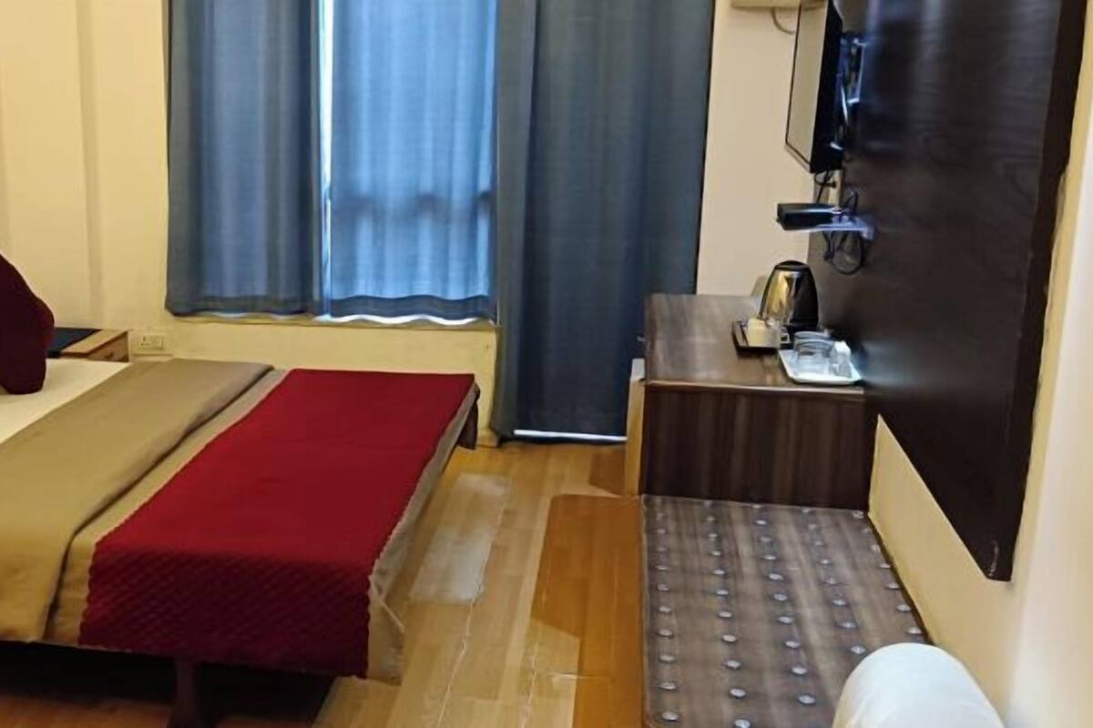 A hotel room with a bed, a desk, a chair, a TV, and a window with curtains.