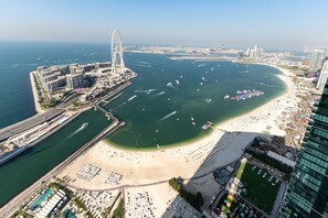 Vue aérienne d’une ville côtière, avec une grande roue bien visible, un port de plaisance et une plage aménagée avec des transats et des parasols.