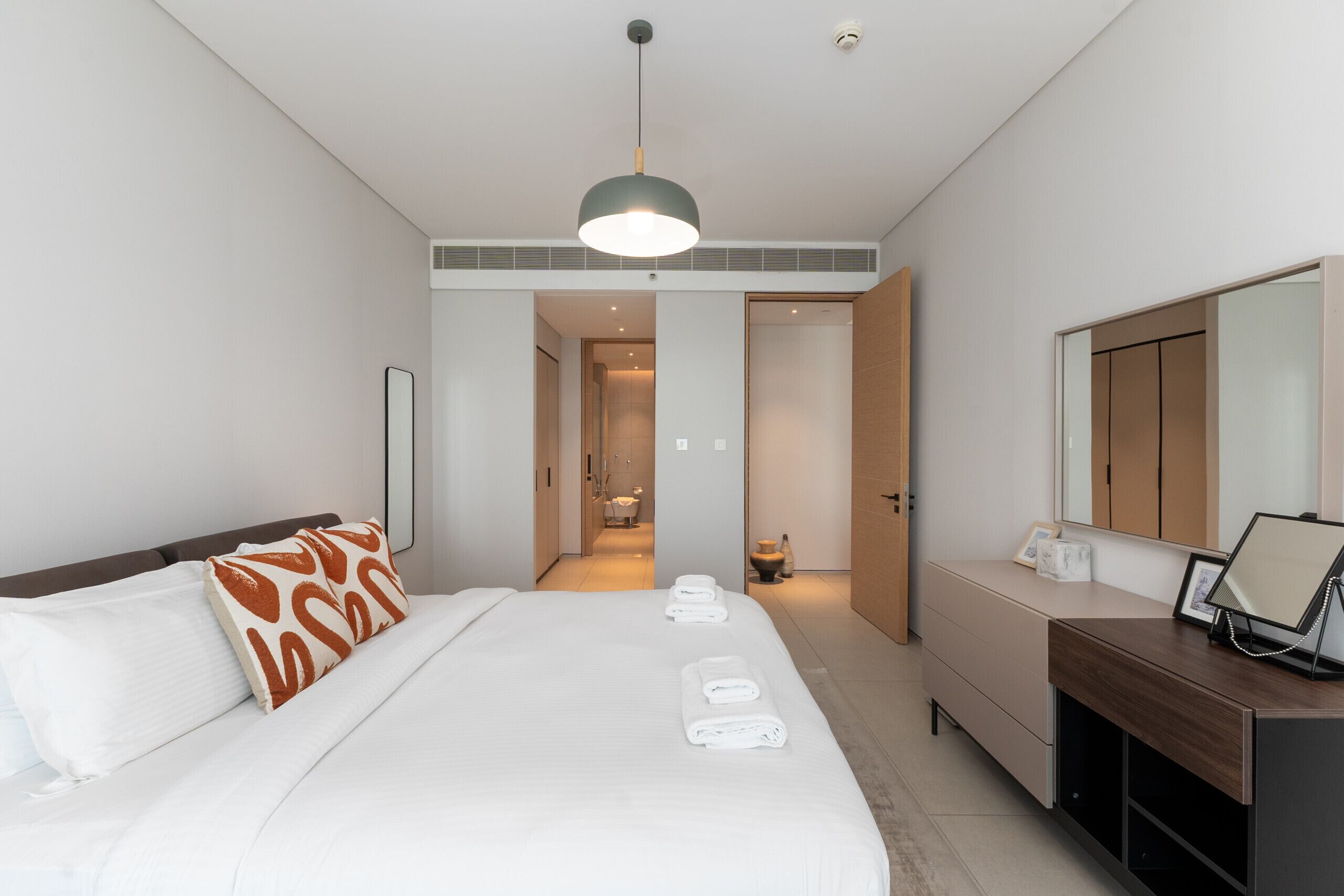 Moderni hotellihuone, jossa on suuri sänky, yöpöytä, peili ja näkymä kylpyhuoneeseen.