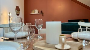 Un coin repas avec une table dressée pour le repas, un luminaire au plafond et un mur orné d’une étagère sur laquelle sont disposés des objets décoratifs.