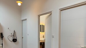 Un couloir doté d’un plancher en bois, un coin repas avec une table et des chaises, et une porte donnant sur une salle de bain équipée d’un lavabo et d’étagères.