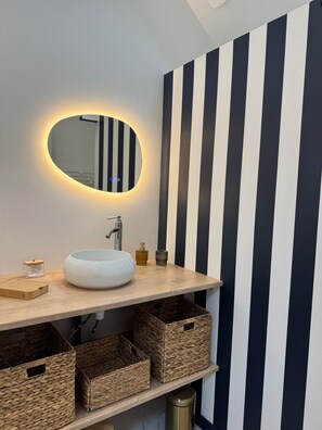 Un baño moderno con un espejo redondo, un lavabo blanco y decoración de pared a rayas.