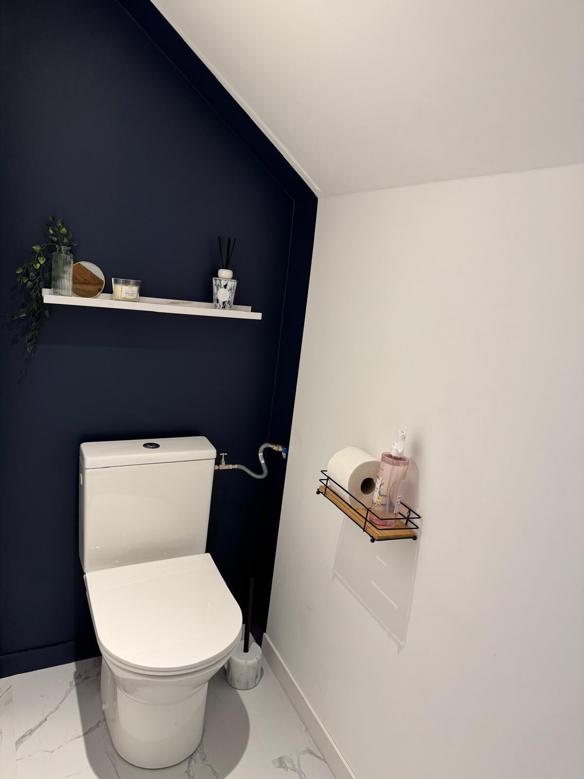 Een moderne badkamer met een wit toilet, donkerblauwe wanden en een marmeren vloer. Er staan planken met toiletartikelen en een toiletrolhouder.