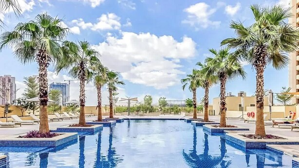 Ein Pool mit Palmen, Liegestühlen und einer Stadtkulisse im Hintergrund.