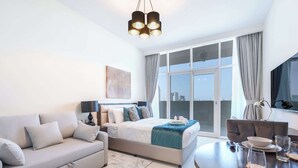 Ein modernes Hotelzimmer mit einem großen Bett, einer Couch, einem Esstisch für zwei Personen und Blick auf die Stadt durch die großen Fenster.